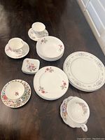 Overall view of mixed floral patterned china plates and cups including the larger dinner plates and smaller bread plates plus a variety of cups and nut dishes.