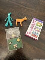Lot contents showing two vintage figures, Tamagotchi sealed box, and Olympic pins in case.