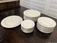 Full set of stacked Noritake plates showing serving, dinner, salad, and bread plates with silver swirl design.