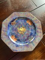 Top-down photo showing the octagonal shape, blue and gold lustre finish, with fruit motifs in center.