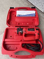 Red RotoZip rotary tool placed inside red plastic case with instruction manual on the lid.