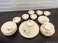 All items arranged on table showing 2 dinner plates, 5 salad plates, 7 bowls, 8 saucers and 8 cups with floral design on cream ceramic.