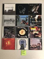 Top-down image showing 12 CD cases arranged in a grid, revealing album covers from various electronic artists including The Postal Service and The Prodigy.