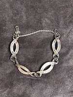 Full view of the vintage silver coin bracelet showing four textured oval links connected by chain links with a safety chain attachment and toggle clasp.