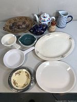 Full collection of vintage and antique ceramic and stoneware kitchenware on a table including platters, bowls, teapot, pitcher, and small jug