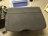Top side of black rear parcel shelf cargo cover showing smooth fabric surface with slight dusting.