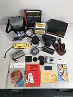 Wide shot showing all photography items laid out on table: cameras, books, straps, boxes and small accessories
