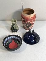 Four pottery items displayed together: swirled vase, green bud vase, blue oil lamp, redware bowl