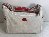 Front view of tan fabric handbag with red leather trim and handle padding with silver studs