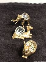 Front view of all three animal figurines (elephant, camel, bunny) showing gold tone and clear faceted crystals in body, on black fabric background.