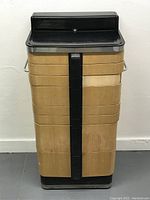 Front view of the vintage American Cabinet Co. Art Deco dentist chest of drawers showing enameled black top, wood laminate drawers with black vertical central trim and chrome side handle.