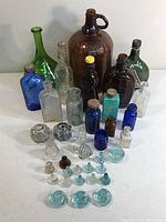Full lot showing assorted vintage and antique bottles in various colors and sizes, and glass stoppers arranged in front.