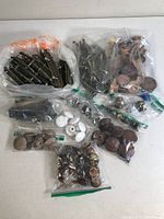Bags of assorted vintage furniture knobs and pulls made of metal, wood, ceramic, and glass, showing wear and rust.