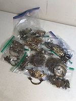 Various vintage and antique ornamental pulls and handles in plastic bags, showcasing different sizes and designs with visible rust and wear
