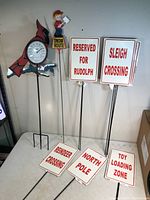 Photo showing metal cardinal thermometer, vintage plastic boy shoveling sign, and multiple Christmas-themed metal yard signs with red text on white background.