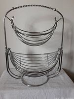 Front view of the chrome metal rack showing two hammock-style baskets suspended one above the other in a curved frame.