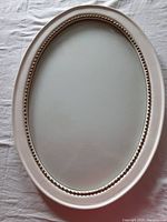 Top-down view of antique painted oval wood frame showing smooth white paint finish and inner beaded detailing under curved glass.