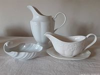 Four white serveware pieces including pitcher, gravy boat with underplate, shell-shaped dish, Mikasa saucer
