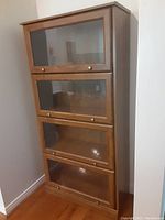 Front view of the closed barrister style MDF bookcase showing four stacked glass doors with metal knobs and wood grain finish.