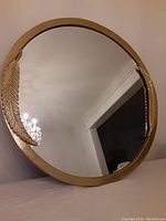 Front view of the round mirror showing the brass frame and two large brass feathers on opposite sides.