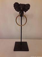 Front view of the bronze elephant head towel rack, showing the full piece with granite base, metal rod, and brass ring.