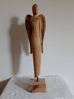 Front view of carved wood angel showing full height and shadow on wall