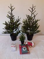 Photo of three faux Christmas trees (two large, one small), Sunbeam timer, battery mini lights and plush puppy ornament on table against white background.