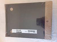 Black-brown KALLAX storage insert box wrapped in plastic, showing front and top sides with holes for fitting shelf supports. Label with Ikea article number 602.781.70 visible.