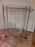 Full view of metal kitchen cart with two wire shelves and a white top shelf, mounted on caster wheels.