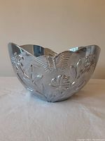 Silver-tone metal salad bowl with scalloped rim and embossed butterfly and floral pattern all around the exterior.
