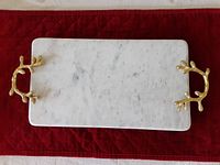 Top view of white marble tray with brass twig-shaped handles on a red quilted surface