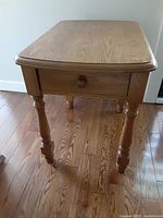 Front-side view showing the drawer with wooden knob and turned legs. Wood grain and some scratches are visible on the table surface.