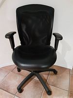 Front view of the black office chair showing padded seat, adjustable armrests, and base with five caster wheels on tiled floor.