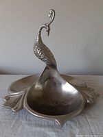 Front angled view of the peacock metal serving dish showing the peacock figure and the bowl with visible wear inside the bowl.