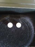 Top-down view showing the front face of the pair of round white freshwater pearl stud earrings on black velvet.