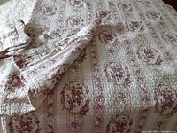 Full view of the queen size quilt made of floral fabric in pink and beige, showing quilted texture and part of the backing fabric turned over.