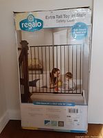 Damaged retail box showing Regalo Extra Tall Top of Stair Safety Gate with a child and adult visible through the bars.
