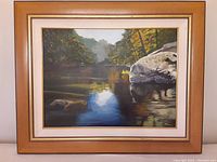 Front view of the framed acrylic painting showing river scene with rocks and trees.