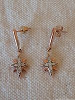 Front view of pair of rose gold star-shaped diamond earrings with butterfly backs on light fabric.