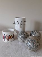 Photo showing two ceramic vases, one face vase with wire glasses and one bird print vase, along with three cherub decorative ceramic balls on surface
