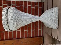 White wicker fern stand leaning on brick wall, showing entire piece lengthwise