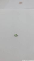 Pear-shaped bright green sapphire gemstone on a plain white background showing the facet cut and shape clearly.