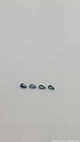 Four pear-shaped blue teal sapphires arranged in a row on a plain grey background.