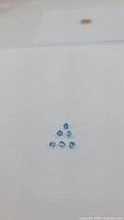 Six calibrated trillion cut Swiss blue topaz gemstones arranged in triangular formation on white background, showing size and cut details.