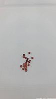 Parcel of small round orange-red diamond cut garnet gemstones scattered on white background.