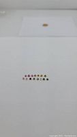 Line of 14 small round faceted rainbow tourmaline stones arranged in order of varying colors from pinks to greens and yellows on white background.