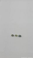 Three oval cut natural green sapphire gemstones arranged horizontally on white background, showing varying green hues and clarity.