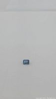 Natural London blue topaz gemstone placed on a plain neutral background, displaying rich blue color and emerald cut shape clearly.