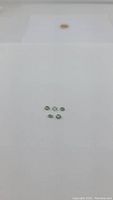 Photo showing five small, oval bright mint green gemstones arranged on a white surface showing color and size.