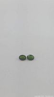Close-up photo showing two matching oval green chrome diopside gemstones with clear visibility of color and cut.